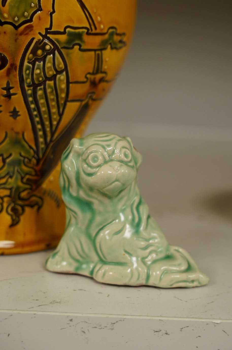 A Brannam yellow vase with stylised decoration of a standing owl with a background of the moon, clouds and three stars, 21cm high, and a Brannam, Barnstaple, a shade of green stylised sitting Dog of Fo, 7.5cm high. Condi